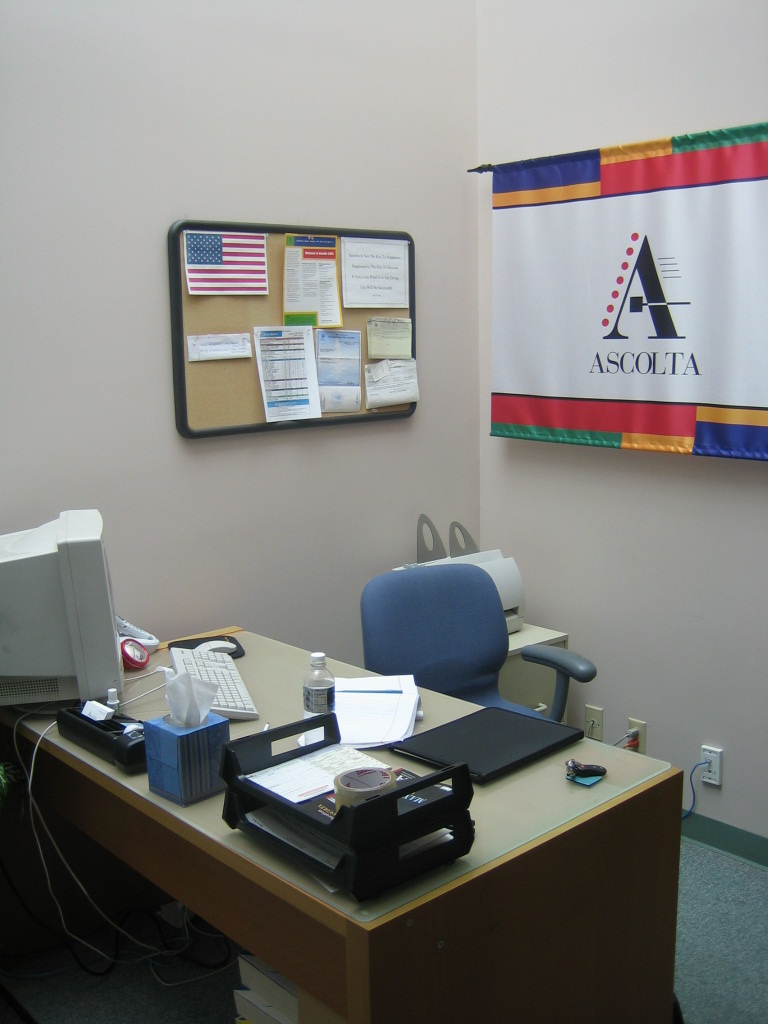 A picture of the Ascolta training office in 2005 with a banner behind the desk showing the Ascolta logo.